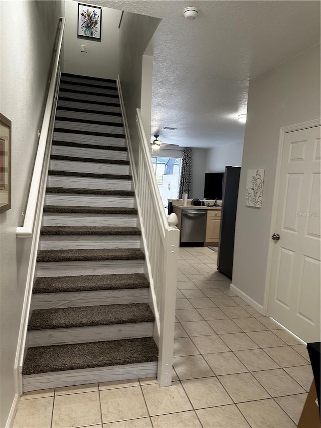 stairway featuring tile patterned flooring, ceiling fan, and a textured ceiling