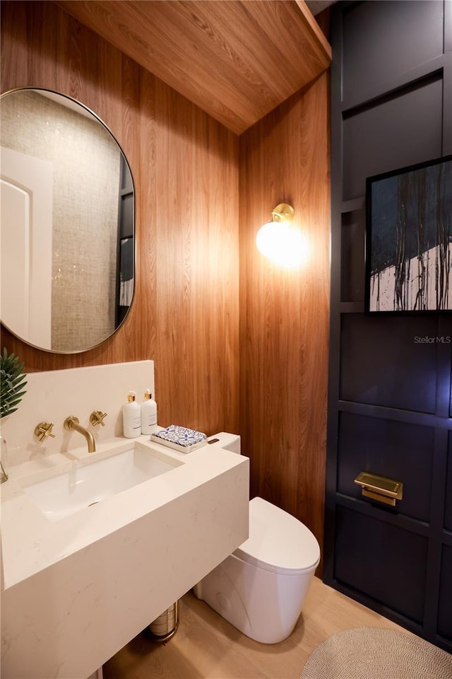 bathroom with toilet, wood ceiling, wooden walls, and sink