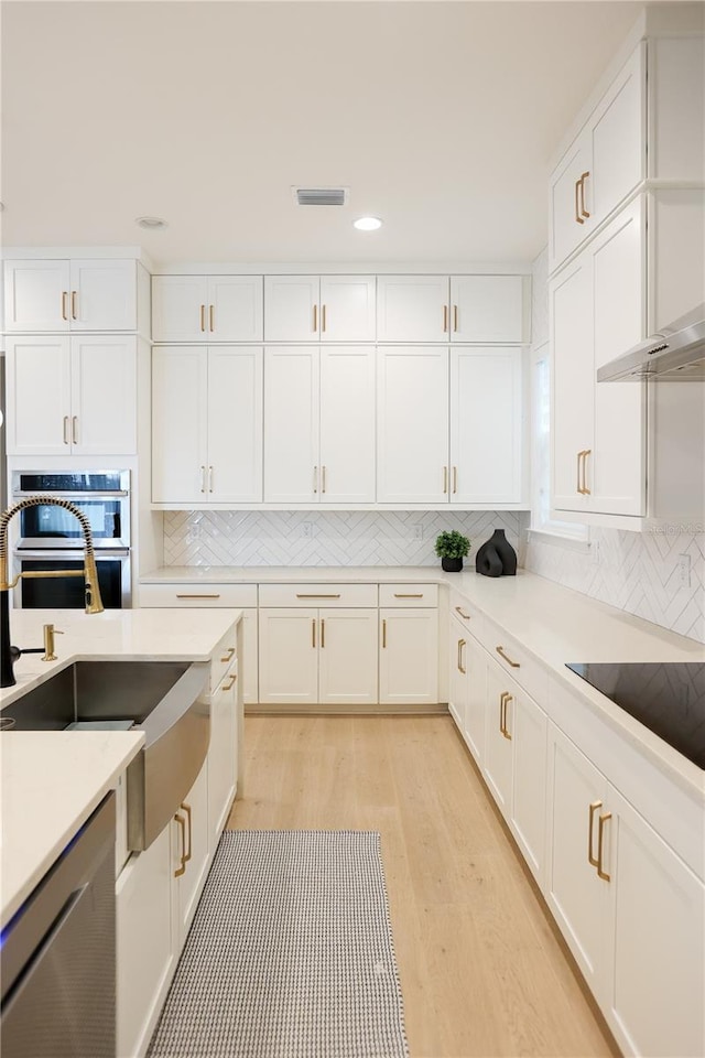 kitchen featuring white cabinetry, stainless steel appliances, tasteful backsplash, and light wood-type flooring