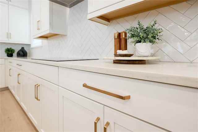 room details with light stone counters, white cabinets, black electric stovetop, and backsplash