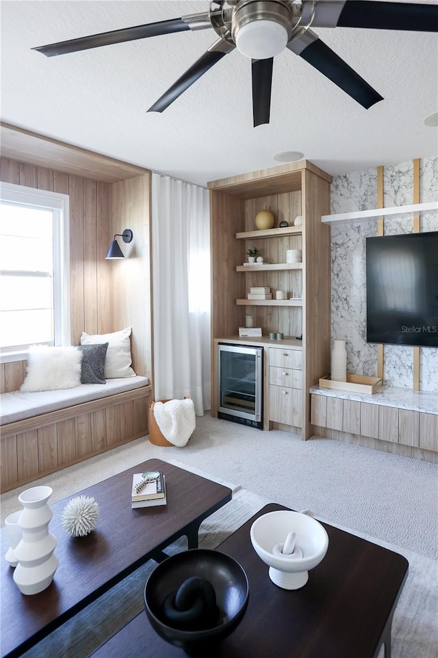 living room with wood walls, a textured ceiling, ceiling fan, beverage cooler, and carpet