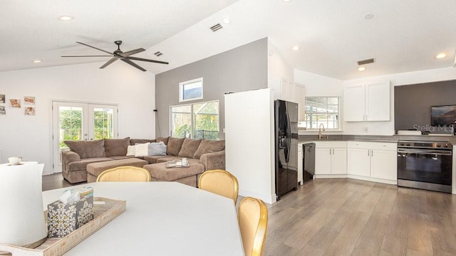 interior space featuring lofted ceiling, sink, white cabinetry, black appliances, and light hardwood / wood-style floors