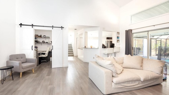 living room with a towering ceiling, a barn door, and light wood-type flooring