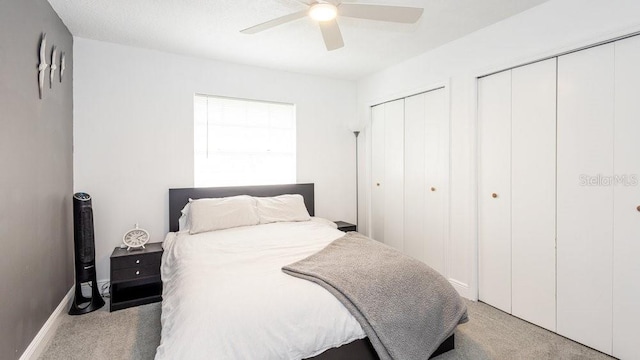 bedroom with light carpet, two closets, and ceiling fan