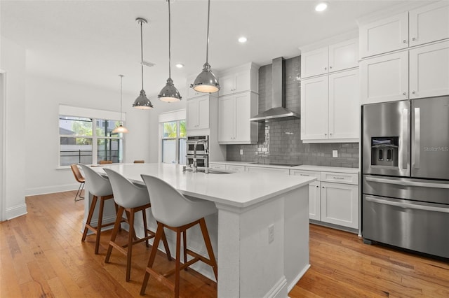 kitchen featuring white cabinetry, wall chimney range hood, a center island with sink, and appliances with stainless steel finishes