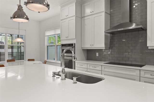 kitchen with white cabinets, hanging light fixtures, stainless steel double oven, black electric cooktop, and wall chimney exhaust hood