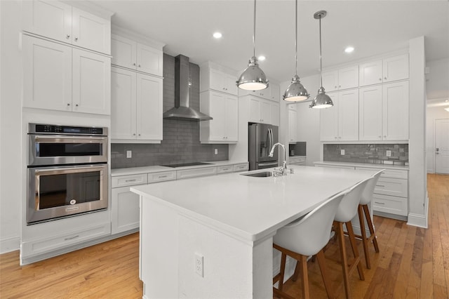 kitchen with white cabinetry, sink, a kitchen island with sink, stainless steel appliances, and wall chimney exhaust hood