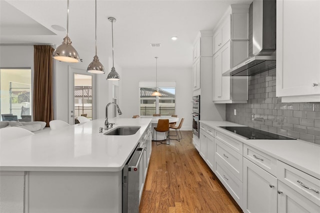 kitchen featuring an island with sink, appliances with stainless steel finishes, sink, and wall chimney range hood