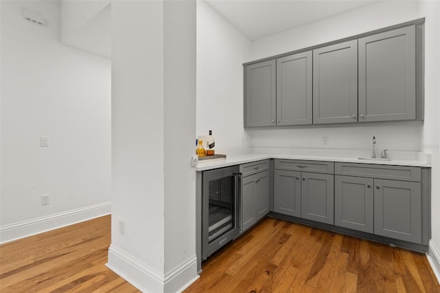 bar featuring light wood-type flooring, beverage cooler, sink, and gray cabinetry