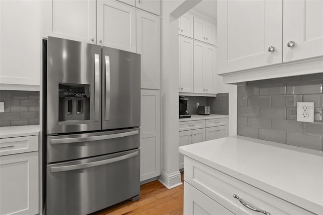 kitchen with stainless steel fridge with ice dispenser, decorative backsplash, white cabinets, and light wood-type flooring