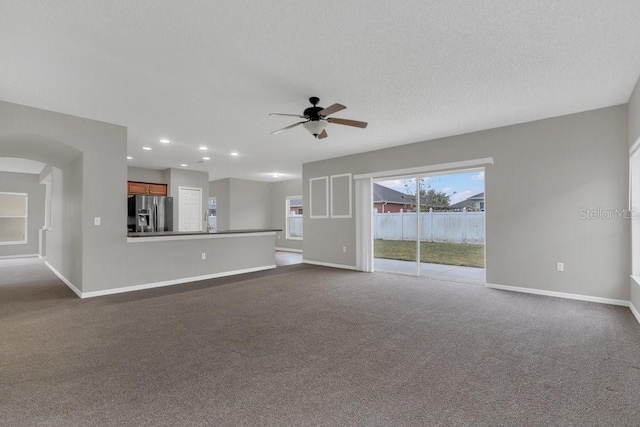 unfurnished living room with a textured ceiling, ceiling fan, and dark colored carpet