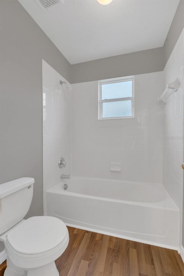 bathroom with hardwood / wood-style flooring, tiled shower / bath, and toilet