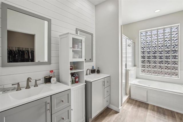 bathroom with wood-type flooring, separate shower and tub, vanity, and wood walls