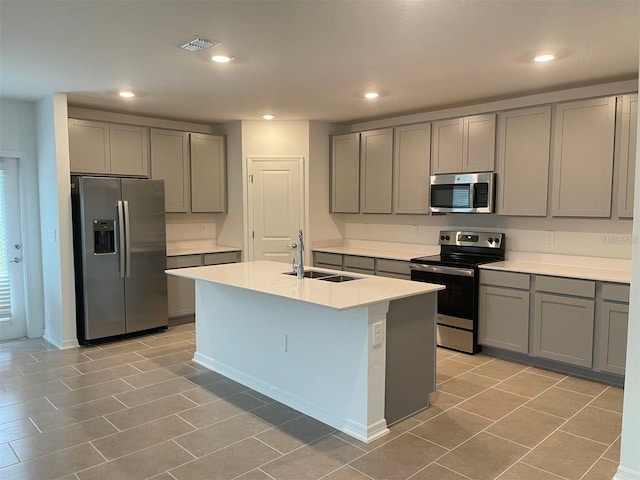 kitchen with a kitchen island with sink, sink, gray cabinets, and appliances with stainless steel finishes