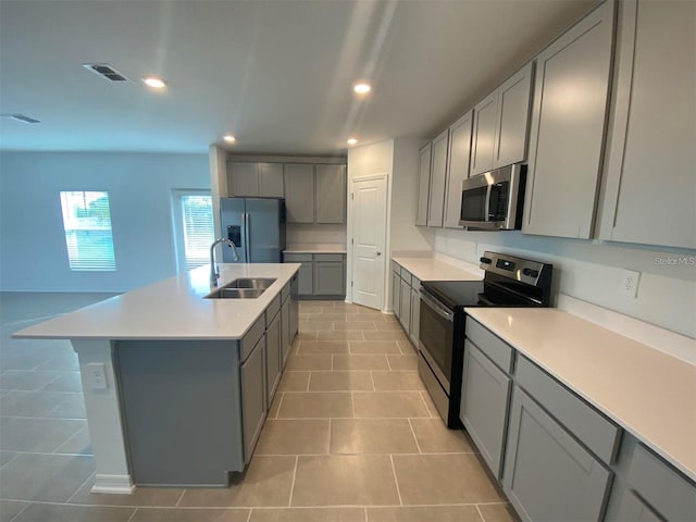 kitchen with appliances with stainless steel finishes, an island with sink, sink, gray cabinetry, and light tile patterned floors