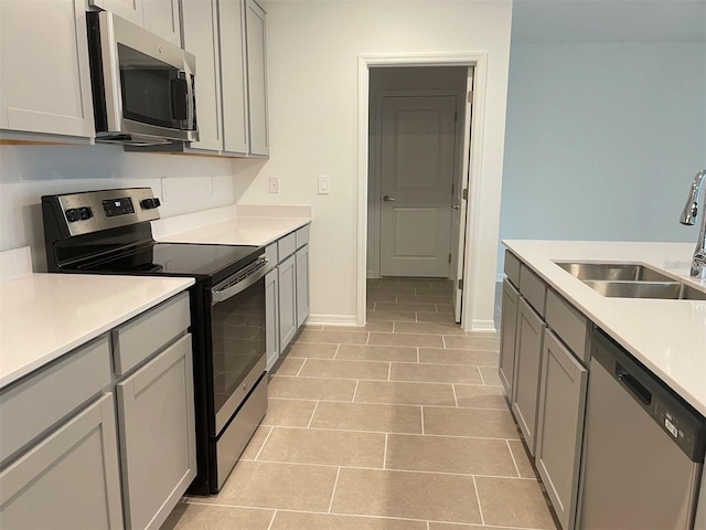 kitchen featuring gray cabinetry, sink, light tile patterned floors, and stainless steel appliances