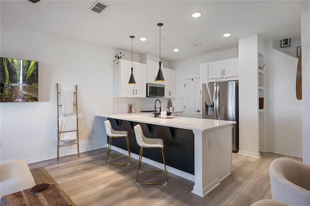 kitchen featuring a breakfast bar area, decorative light fixtures, kitchen peninsula, stainless steel appliances, and white cabinets