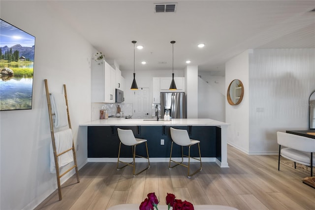 kitchen featuring white cabinetry, hanging light fixtures, appliances with stainless steel finishes, a kitchen breakfast bar, and kitchen peninsula