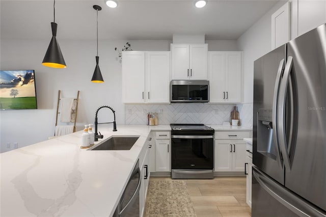 kitchen with sink, white cabinetry, stainless steel appliances, light stone countertops, and decorative light fixtures