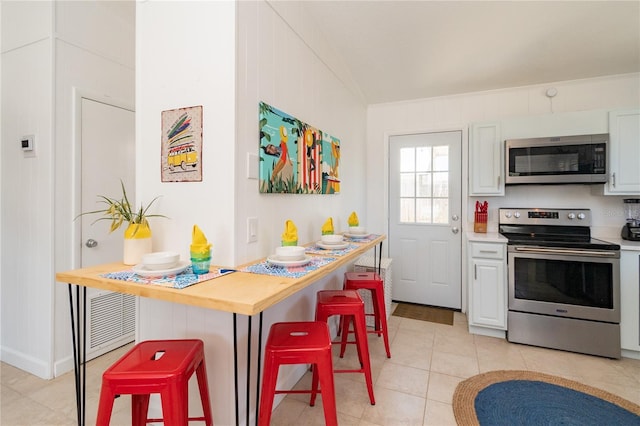 kitchen with white cabinetry, stainless steel appliances, crown molding, and a breakfast bar area