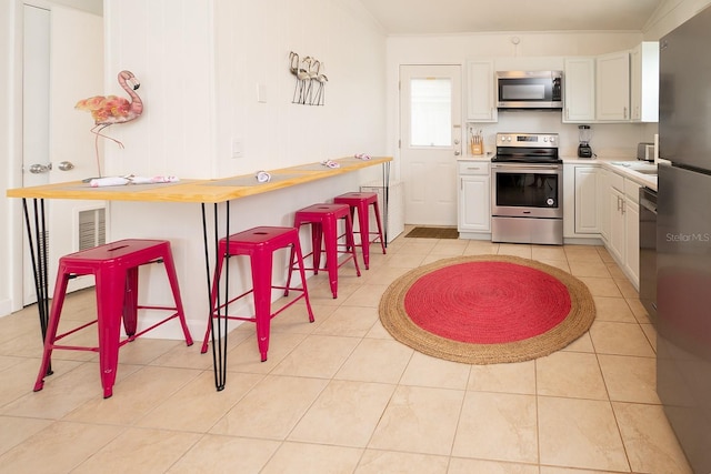 kitchen featuring white cabinetry, appliances with stainless steel finishes, a breakfast bar area, and light tile patterned floors