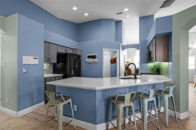 kitchen with a breakfast bar, sink, black fridge with ice dispenser, light tile patterned floors, and kitchen peninsula