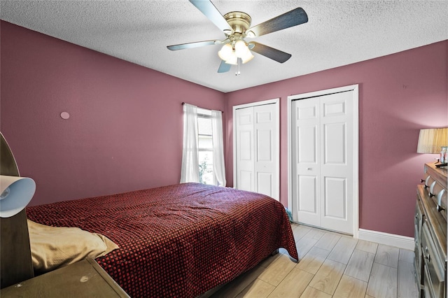 bedroom featuring ceiling fan, two closets, a textured ceiling, and light wood-type flooring