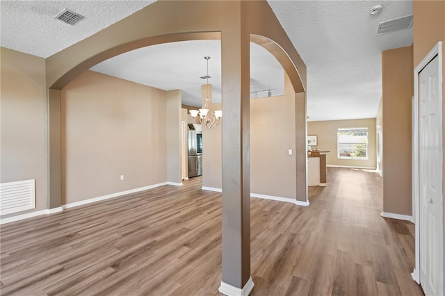 unfurnished living room featuring a notable chandelier, light hardwood / wood-style floors, and a textured ceiling