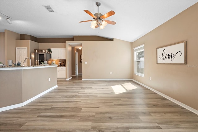 unfurnished living room featuring lofted ceiling, sink, ceiling fan, a textured ceiling, and light wood-type flooring