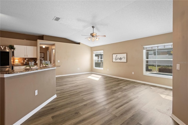 unfurnished living room with ceiling fan, wood-type flooring, vaulted ceiling, and a textured ceiling