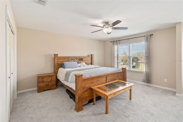 bedroom featuring ceiling fan, light colored carpet, a closet, and a textured ceiling