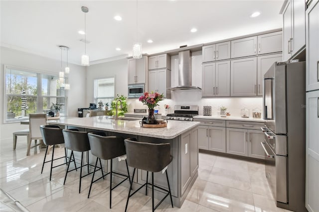 kitchen featuring pendant lighting, a kitchen island with sink, light stone counters, stainless steel appliances, and wall chimney range hood