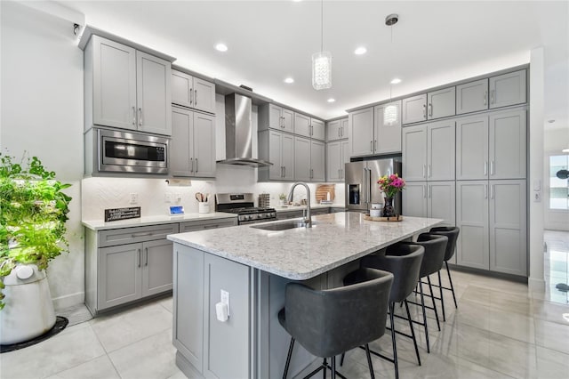 kitchen featuring wall chimney exhaust hood, sink, gray cabinetry, light stone counters, and appliances with stainless steel finishes