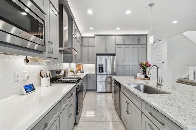 kitchen featuring sink, wall chimney range hood, stainless steel appliances, tasteful backsplash, and decorative light fixtures