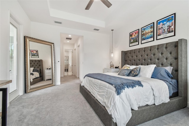 bedroom featuring a raised ceiling, ensuite bathroom, light carpet, and ceiling fan