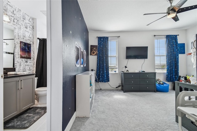 bedroom with ceiling fan, ensuite bathroom, and light carpet