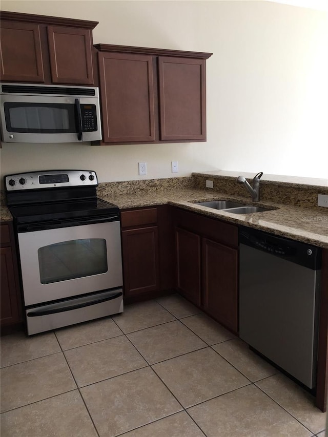 kitchen featuring light tile patterned flooring, sink, dark brown cabinets, dark stone counters, and stainless steel appliances