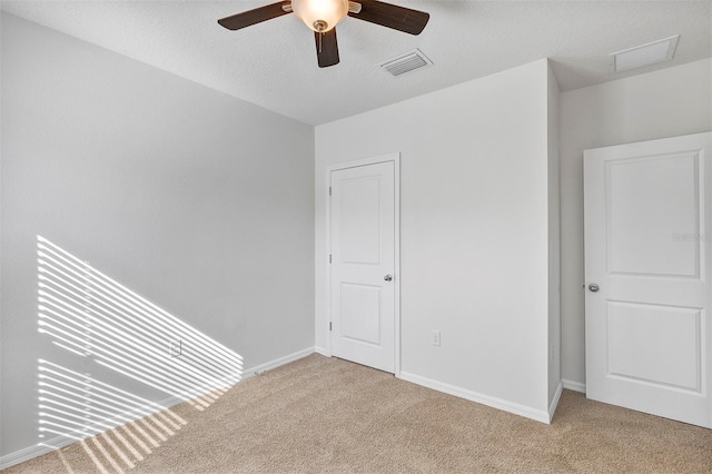 unfurnished bedroom featuring ceiling fan, light colored carpet, and a textured ceiling