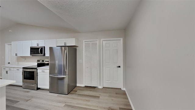 kitchen with white cabinetry, vaulted ceiling, stainless steel appliances, and light hardwood / wood-style floors