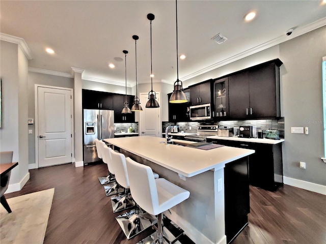 kitchen with a kitchen bar, decorative light fixtures, a center island with sink, stainless steel appliances, and decorative backsplash