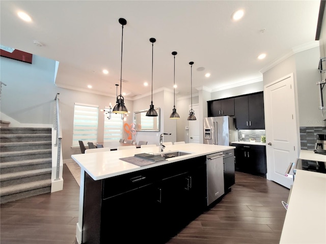 kitchen with sink, stainless steel appliances, tasteful backsplash, an island with sink, and decorative light fixtures