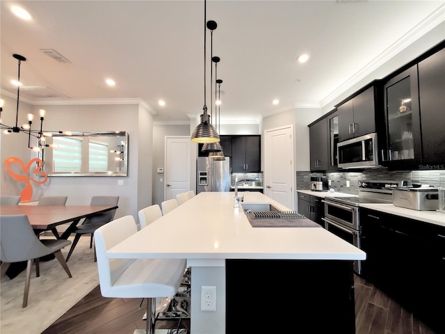 kitchen featuring stainless steel appliances, hanging light fixtures, a kitchen island with sink, and sink