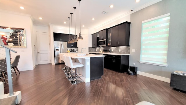 kitchen with a center island with sink, stainless steel appliances, hanging light fixtures, a breakfast bar area, and tasteful backsplash