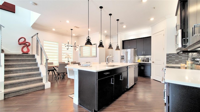 kitchen featuring an island with sink, decorative light fixtures, sink, tasteful backsplash, and appliances with stainless steel finishes