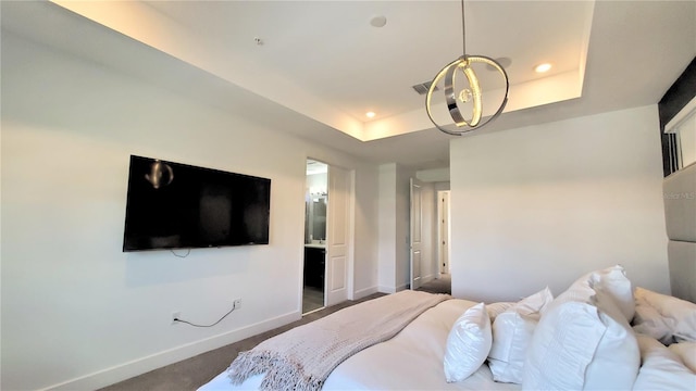 bedroom featuring a tray ceiling, ensuite bathroom, and dark colored carpet