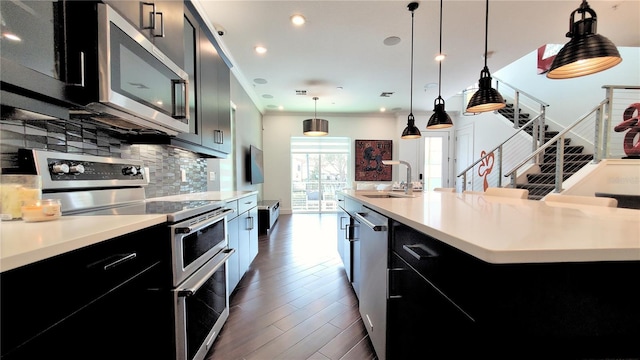 kitchen with a large island, hanging light fixtures, stainless steel appliances, sink, and tasteful backsplash