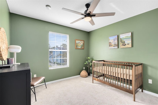 bedroom with light colored carpet, a nursery area, and ceiling fan