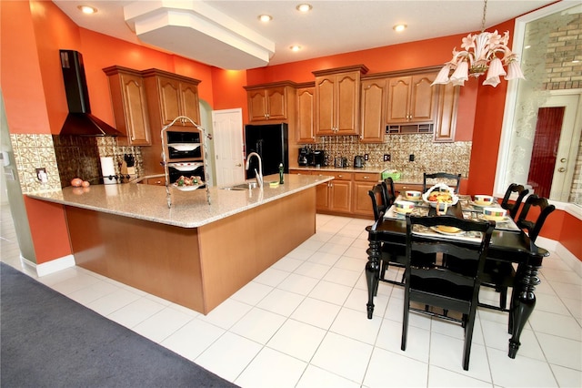 kitchen featuring wall chimney range hood, sink, black refrigerator, light stone counters, and ventilation hood