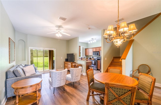 dining space with ceiling fan with notable chandelier and light wood-type flooring