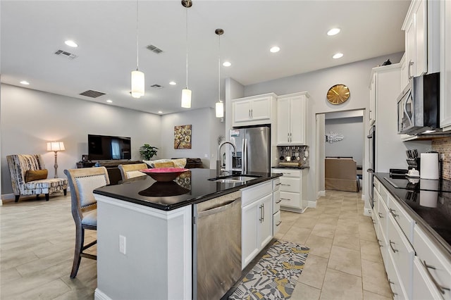 kitchen featuring appliances with stainless steel finishes, hanging light fixtures, a kitchen breakfast bar, an island with sink, and white cabinets